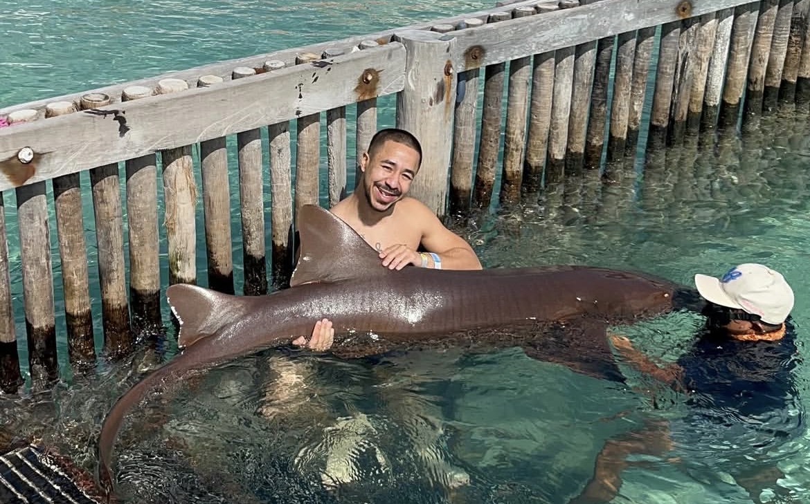 Adrian grinning while holding a nurse shark in clear tropical water